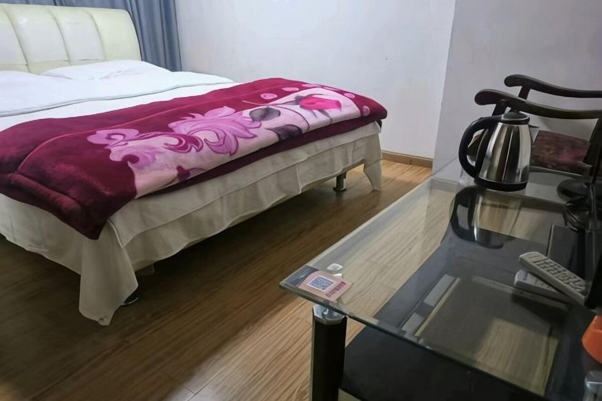 A hotel room with a bed, a glass table with a remote control, and a coffee maker.