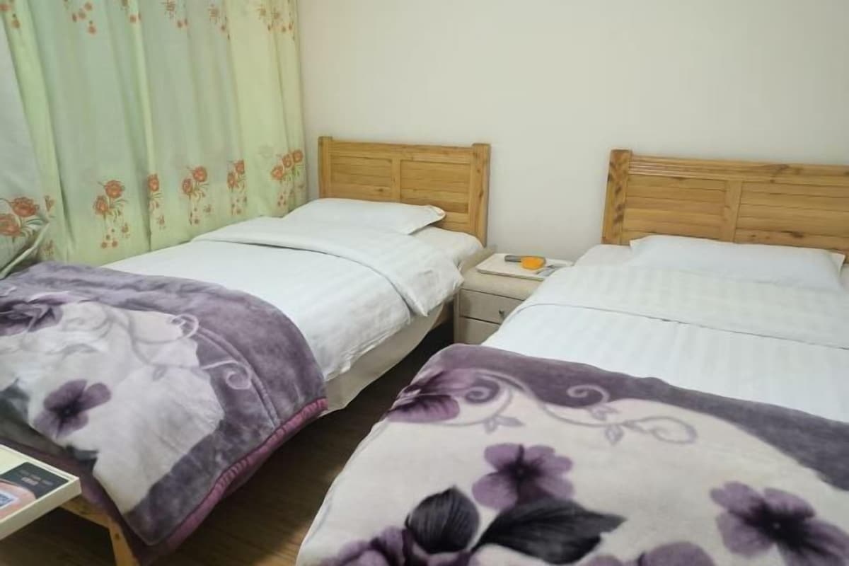 A room with two wooden beds, a nightstand with a lamp, and a floral curtain.