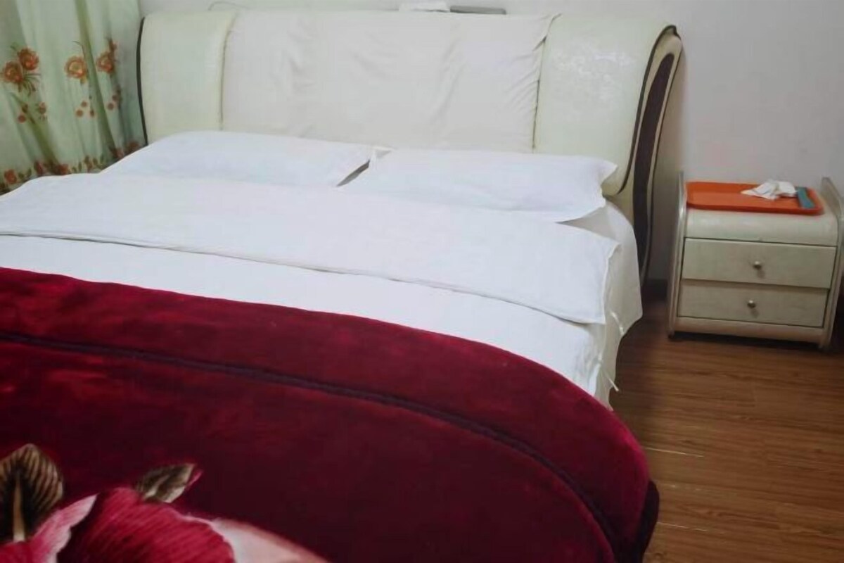 A bed with a white headboard and a red blanket, a nightstand with a lamp, and a drawer unit.