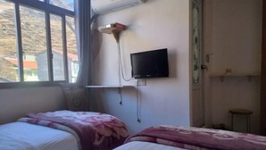 A room with two beds, a TV mounted on the wall, and a window with a view of buildings outside. - Jiangling Inn (Songpan)