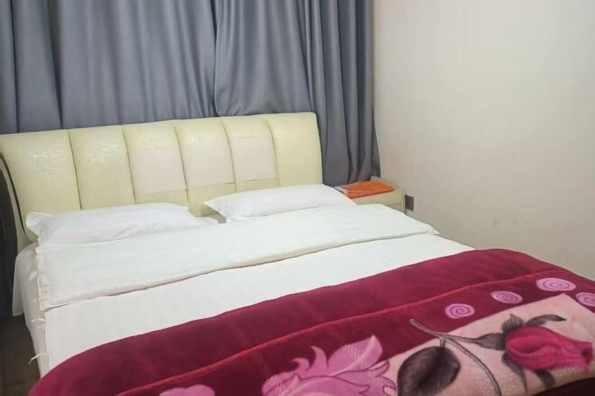 Ein Bett mit Kopfteil, weißer Bettwäsche und einer roten Decke mit floralem Muster.