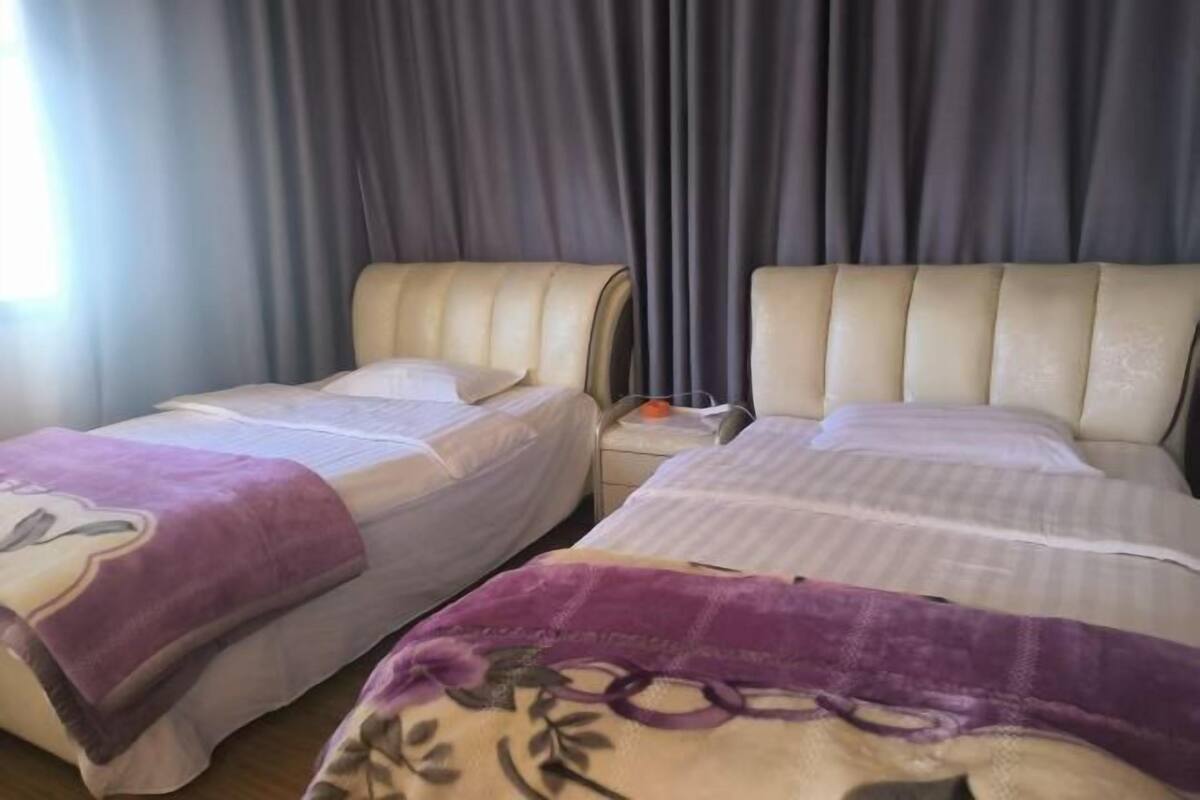 Ein Hotelzimmer mit zwei Betten, einem Nachttisch und einem Fenster mit Vorhängen.
