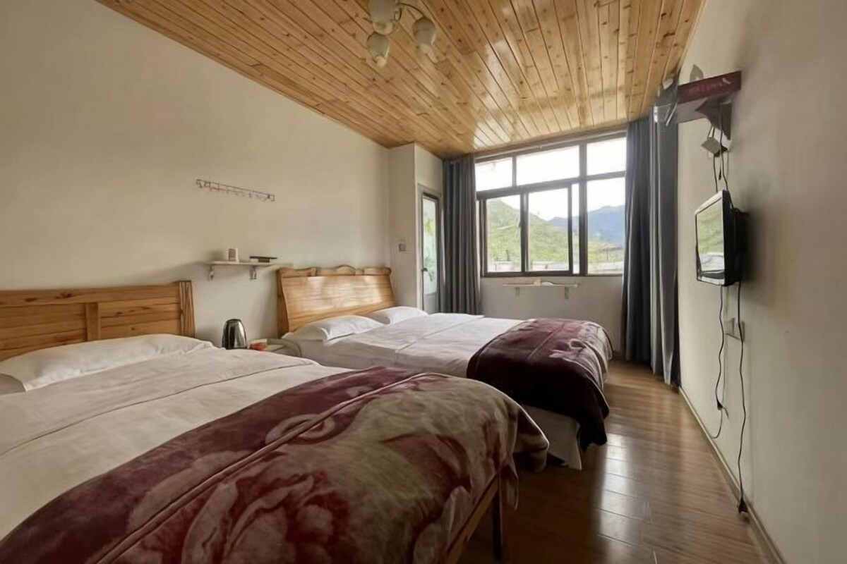 A hotel room with two beds, wooden ceiling, large windows, and a TV.