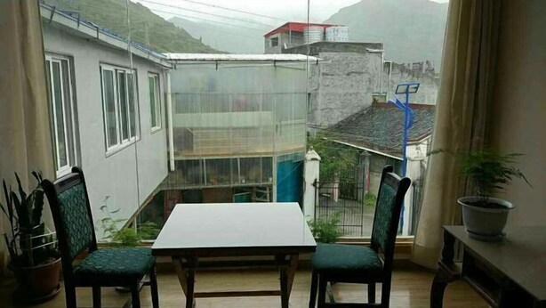 Een klein balkon met een tafel en stoelen, uitkijkend op een woongebied met huizen en een berg op de achtergrond.