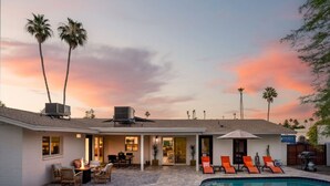 A modern house with a swimming pool, outdoor seating, and palm trees.