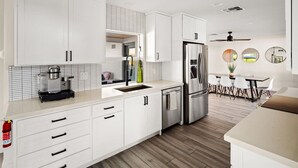 A modern kitchen with white cabinetry, stainless steel appliances, and a dining area with a table and chairs.