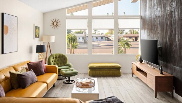 A modern living room with a sofa, green armchair, ottoman, and a TV on a wooden stand.