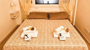 Un lit bien fait, avec une couvre-lit à motifs, deux oreillers et deux serviettes, chacune portant une étiquette avec un nom.