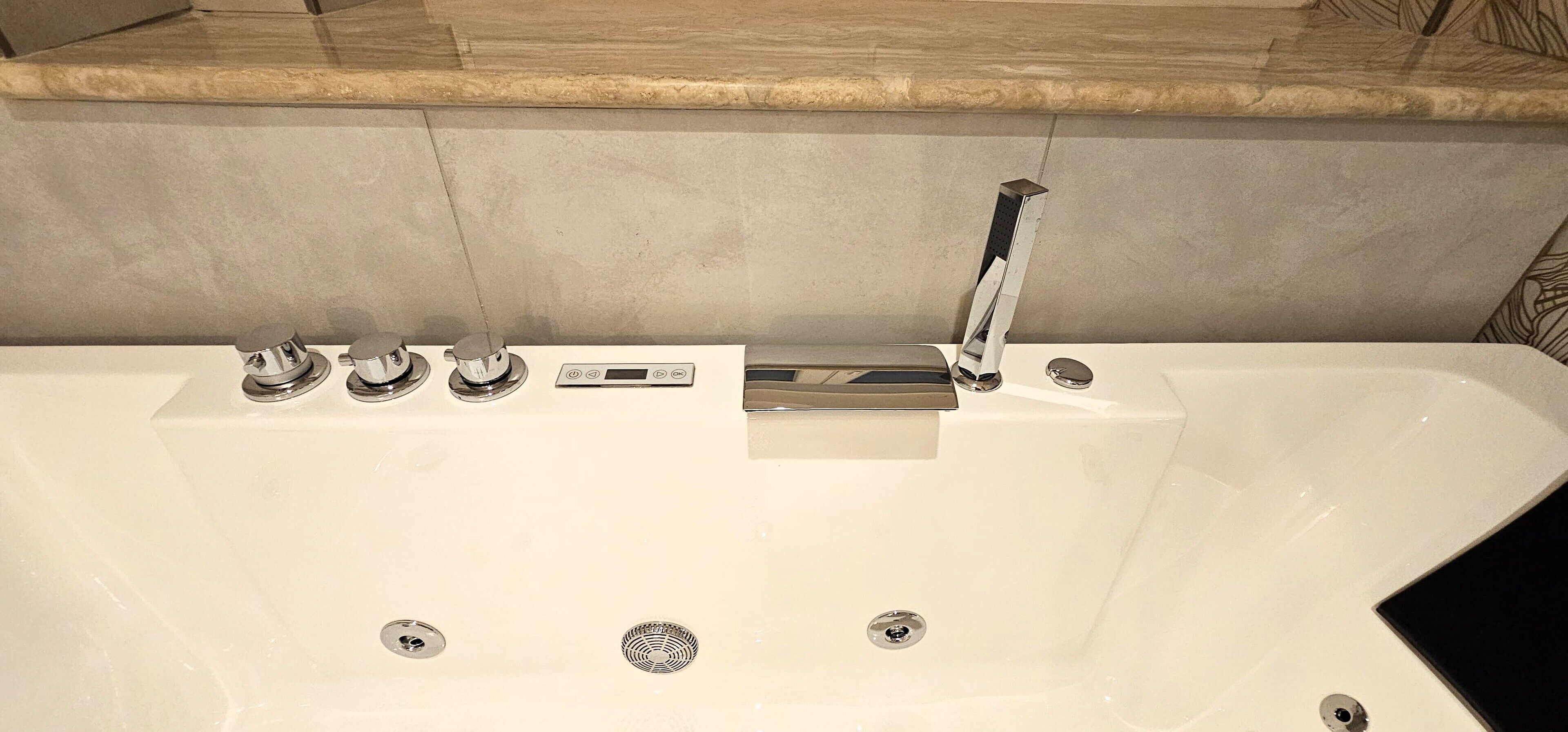 Ein modernes Badezimmer mit einer großen Badewanne, einer Steuerung und einem Wasserhahn.