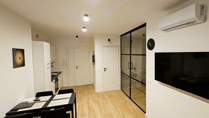 A modern living room with a flat-screen TV, a dining area with a table and chairs, and a glass door leading to a kitchen. - LUX Beach Apartment BLACK (Ostia)