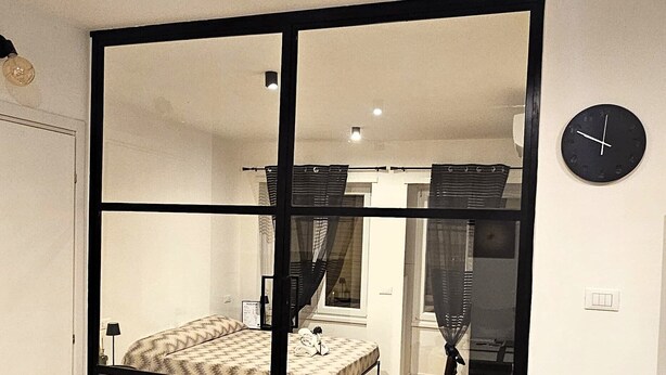 A bedroom with a bed, a mirror, a clock, and a sliding door. - LUX Beach Apartment BLACK (Ostia)