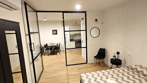 A modern apartment with a dining area, kitchenette, and a bedroom with a patterned bedspread. - LUX Beach Apartment BLACK (Ostia)