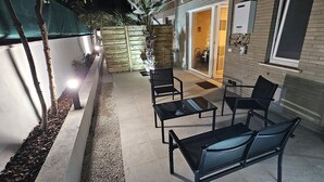 An outdoor seating area with a table and chairs, a wooden fence, and a building entrance. - LUX Beach Apartment BLACK (Ostia)