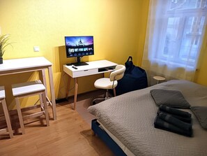 Une chambre d’hôtel avec un lit, un bureau avec un ordinateur, une chaise et une fenêtre avec des rideaux.