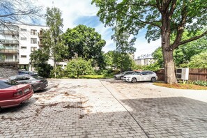 A paved driveway with parked cars, a large tree, and residential buildings in the background. - Peaceful studio with desk & free parking (Tallinn)