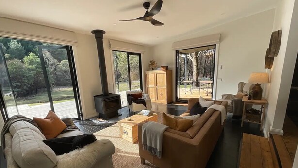 Una sala de estar moderna con un sofá grande, una mesa de centro y una chimenea. Se ve el exterior a través de amplios ventanales.