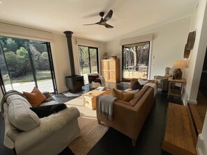Uma sala de estar moderna com um sofá grande, uma mesa de centro e uma lareira. Há vista para o exterior através de grandes janelas.