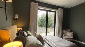 Un dormitorio con una cama, una mesita de noche, una lámpara y vistas al exterior a través de una ventana.