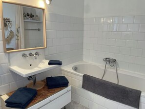 A bathroom with a white sink, mirror, and bathtub. There are towels on the counter and a towel on the bathtub.