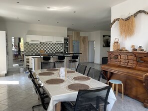 A modern dining area with a large table, black chairs, and a wooden piano.