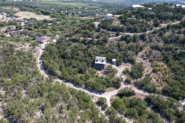 An aerial view of a residential area with a house surrounded by dense vegetation and a winding road.