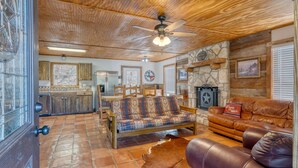 A rustic interior with a stone fireplace, wooden ceiling, and a sofa with patterned cushions.