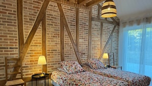 A bedroom with a large bed, wooden beams, brick walls, and a window with curtains.