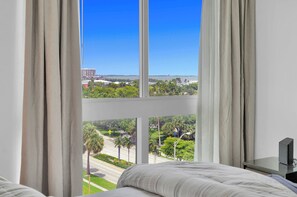 A hotel room with a large window offering a view of a cityscape and greenery.