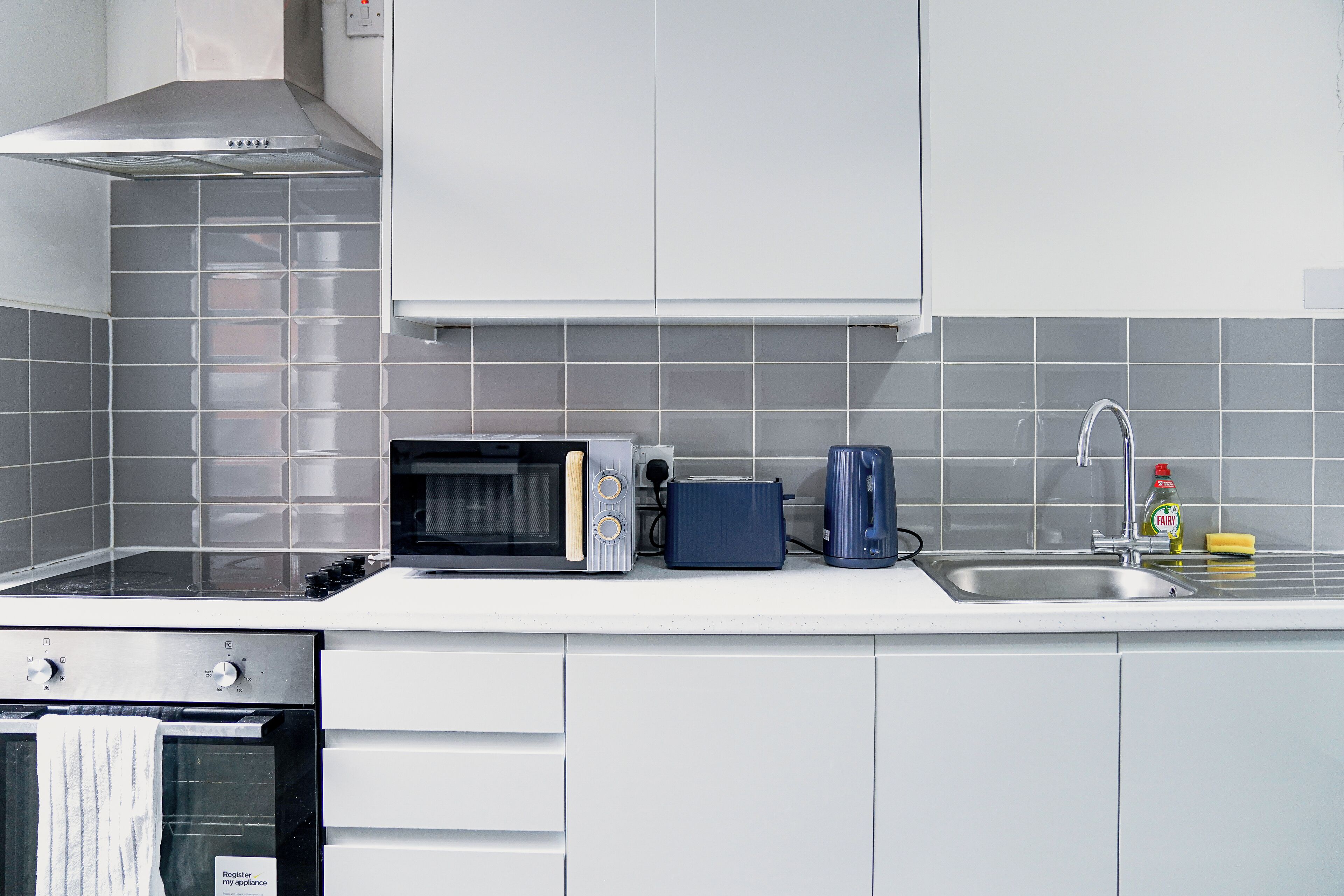 A modern kitchen with a microwave, toaster, kettle, and a sink with a faucet.