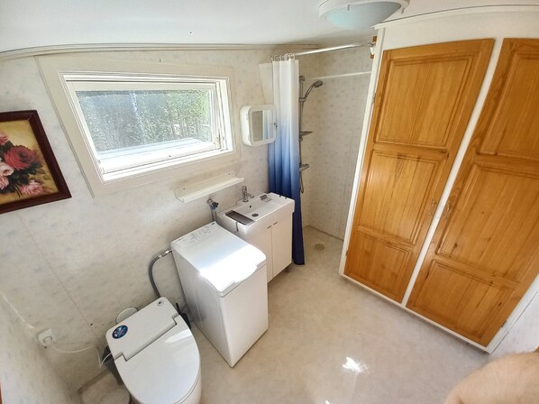 A compact bathroom with a toilet, washing machine, sink, and shower.