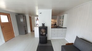 Een knus leefruimte met een kitchenette, een centraal geplaatste open haard, een bank en een houten tafel.