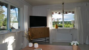 Een kamer met een houten bankje, een flatscreen televisie aan de wand, een tafel met een boek en kaarsen, en een raam met uitzicht op groen.