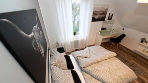 Ein Schlafzimmer mit einem Bett, einem Schreibtisch, einem Stuhl, einem Fenster mit Vorhängen und einem Bild an der Wand.