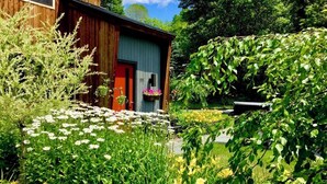Ett trähus med en röd dörr, omgivet av en trädgård med olika sorters blommor och grönska.