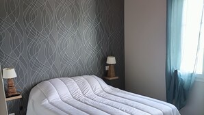 Ein Schlafzimmer mit Bett, Klimaanlage, Wand mit Muster, Nachttischlampen und einem Fenster mit Vorhängen.