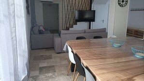 Ein modernes Wohnzimmer mit einem Holzes Esstisch, einem grauen Sofa und einem an der Wand montierten Fernseher.