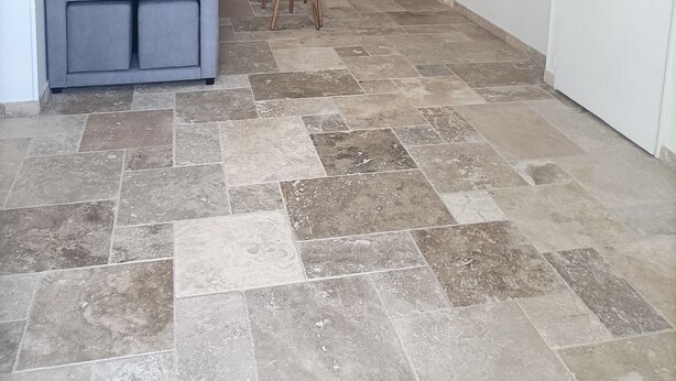 Ein Wohnzimmer mit grauem Sofa, einem kleinen Tisch und einem Sessel. Darüber befindet sich eine Wanddekoration und rechts ein Treppenaufgang.