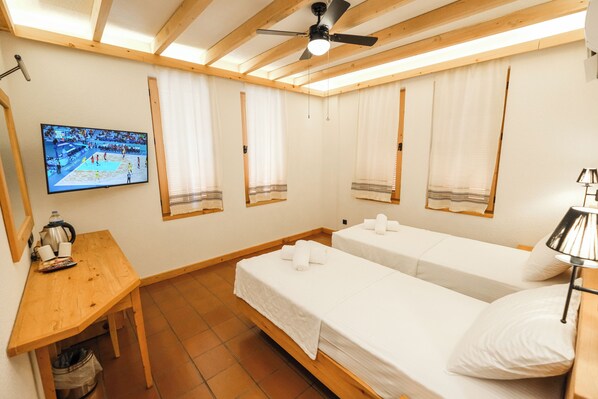 A room with two beds, a wooden table, a TV, and a ceiling fan. - The Cadianda Inn (Fethiye)