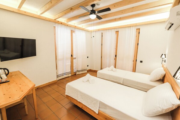 Una camera con due letti singoli, una scrivania in legno, una TV a schermo piatto e una ventola a soffitto.