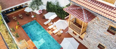 Un área de piscina en la azotea con piscina, tumbonas, sombrillas y una terraza de madera.