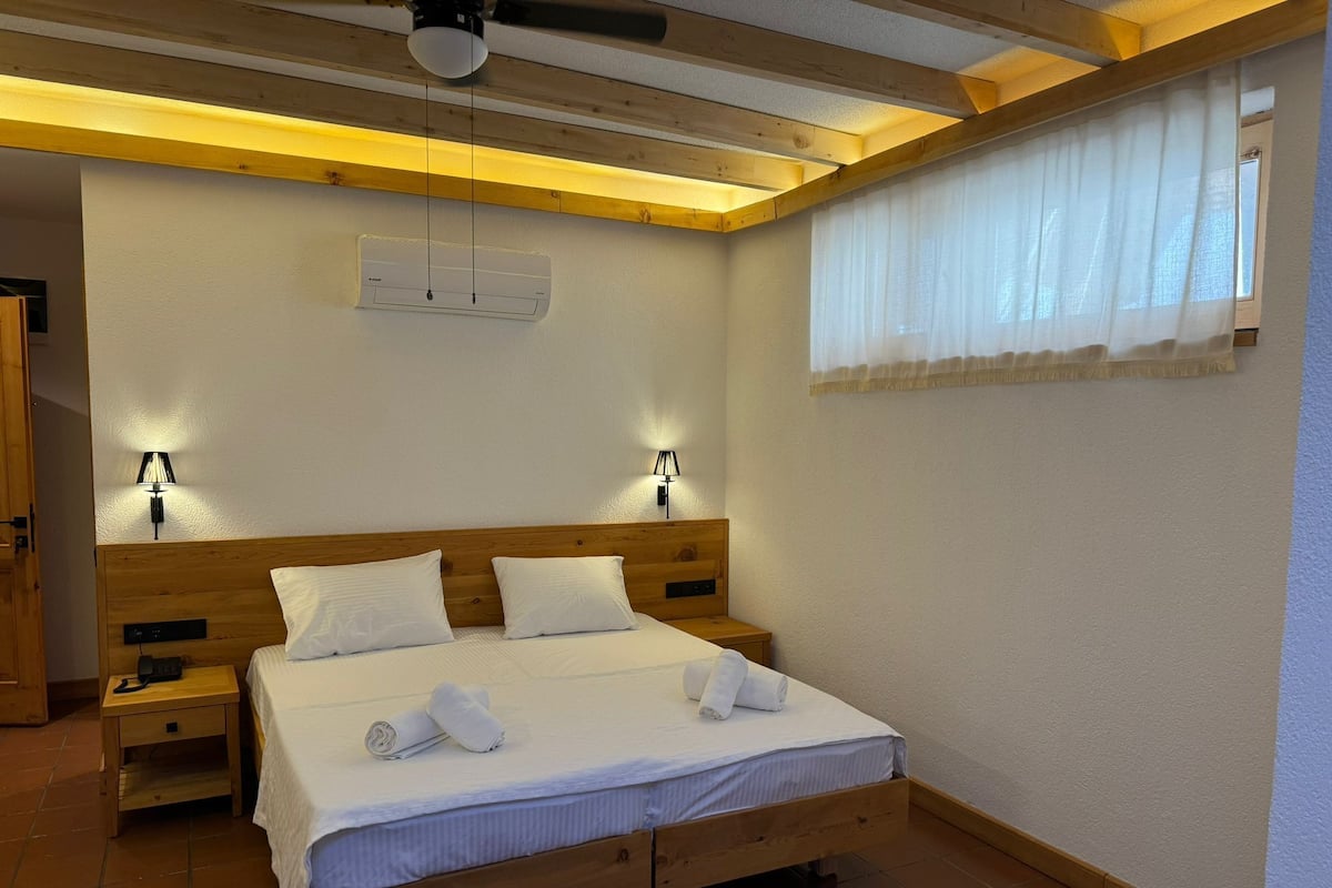 A bedroom with a wooden bed, two bedside tables, a ceiling fan, and a window with sheer curtains.