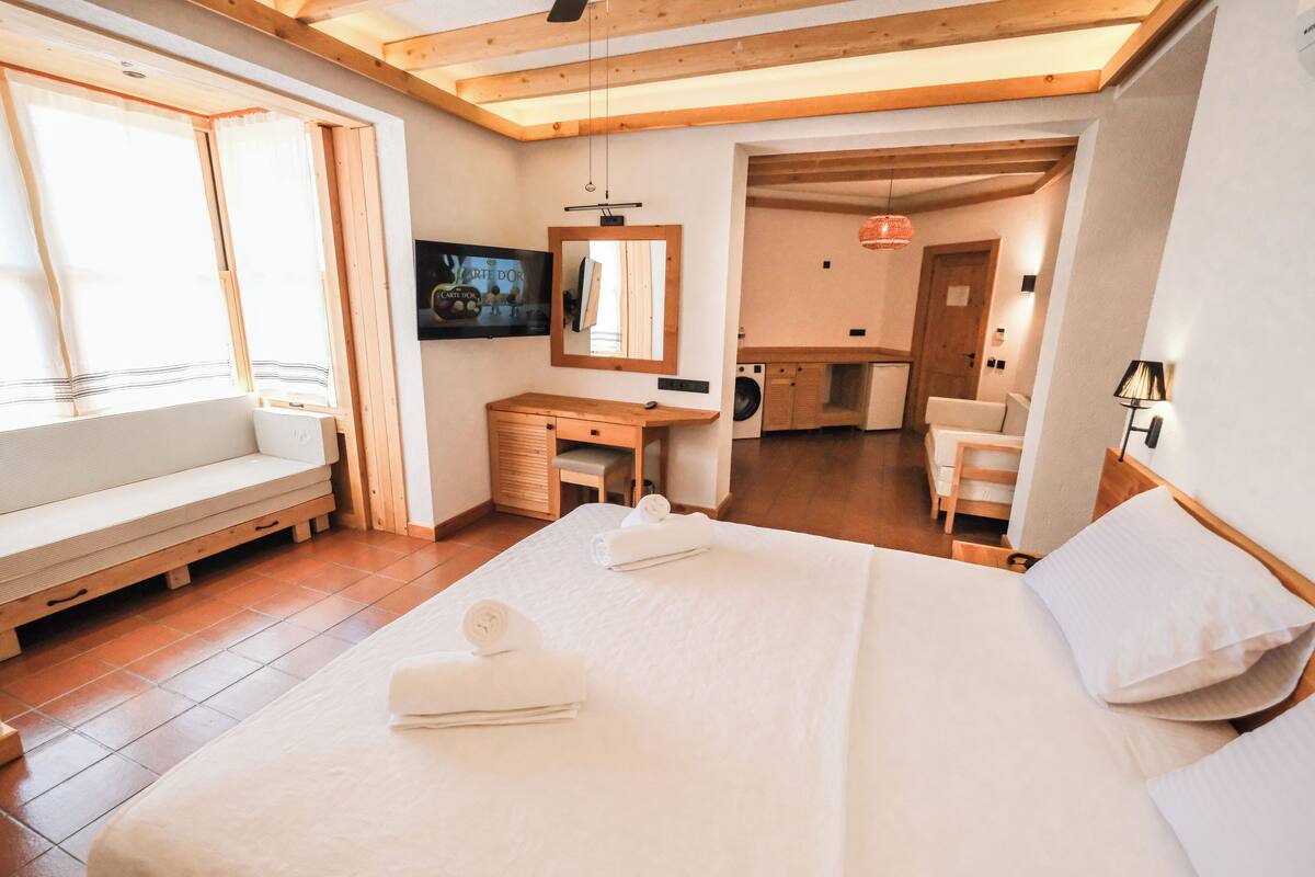 A bedroom with a large bed, a wooden desk, a washing machine, and a seating area with a bench.
