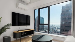 A modern living room with a large window, a flat-screen TV, a round coffee table, and a minimalist entertainment unit. - The Rubik | Designer One-Bedroom in Cape Town (Cape Town)