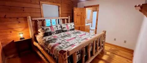 A wooden cabin bedroom with a bed, a nightstand, and a window.