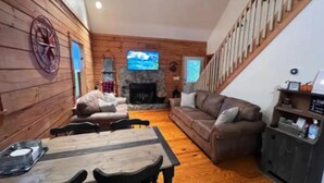 Una sala de estar acogedora con chimenea, paredes de madera, televisor y escalera.