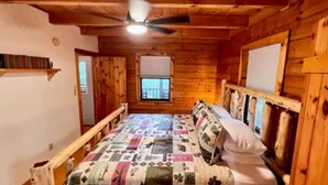 Un dormitorio de cabaña de madera con una cama, un ventilador de techo, una ventana y una puerta.