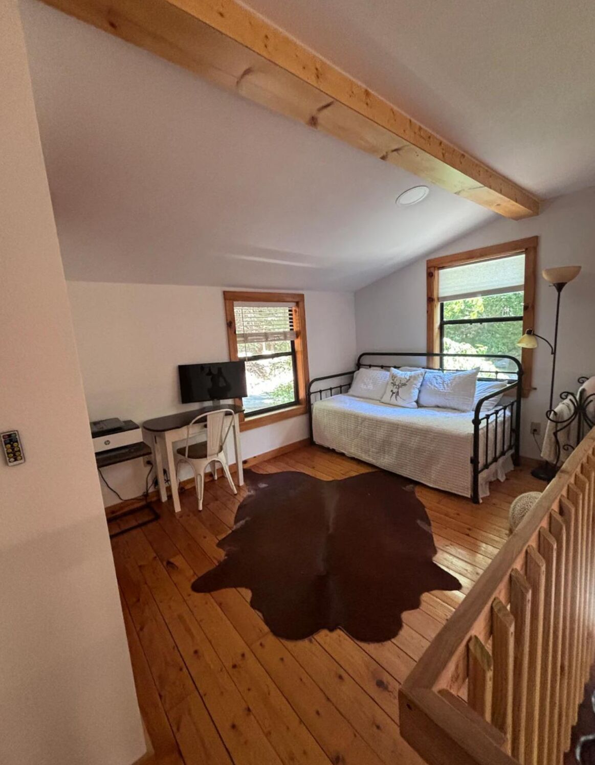 Ein Schlafzimmer mit einem Bett, einem Schreibtisch und einem Stuhl, einem Kuhfellteppich und einem Fenster mit Blick auf Grünflächen.