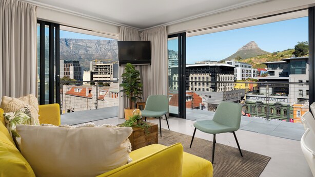 A modern living room with a yellow sofa, a green armchair, and a flat-screen TV mounted on the wall. - Stunning Views From De Waterkant Apartment (Cape Town)