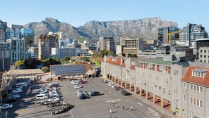 A parking lot with multiple cars, a building with a red roof, and a mountain in the background. - Stunning Views From De Waterkant Apartment (Cape Town)