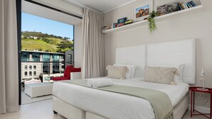 A modern bedroom with a large bed, a red chair, and a view of a cityscape through a large window. - Stunning Views From De Waterkant Apartment (Cape Town)